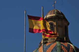 Foto einer im Wind wehenden, spanischen Flagge. Im Hintergrund eine Gebäudekuppel
