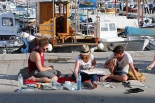 Foto von 3 malenden Personen, sitzend auf dem Boden in einem Hafen